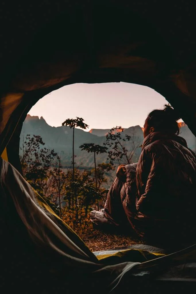 Femme dans son duvet regardant un lever de soleil à Aurère dans le cirque de Mafate sur l’île de la Réunion. 