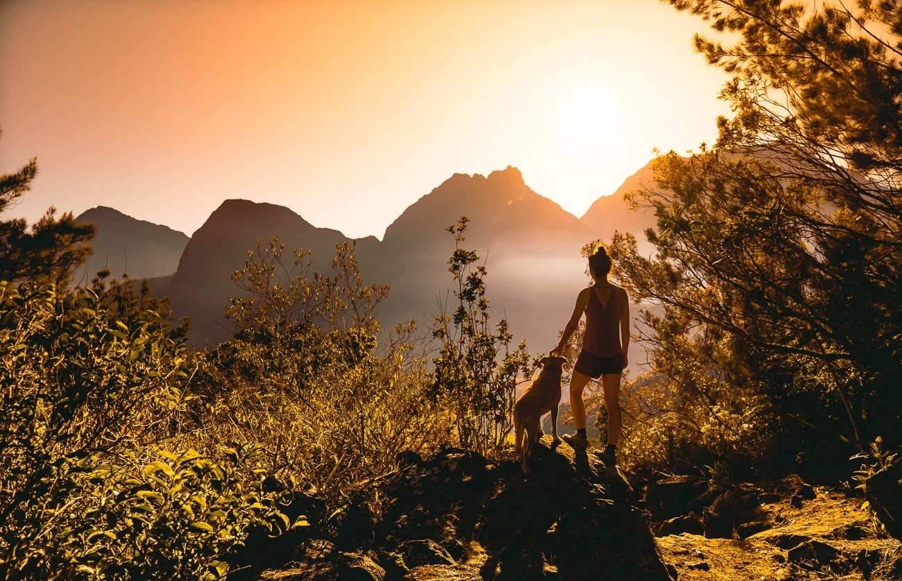 Femme avec un chien devant un lever de soleil dans le Cirque de Mafate.
