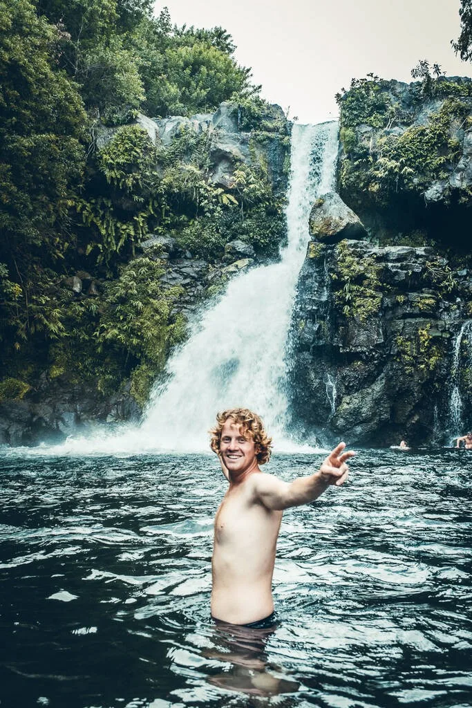Un homme qui écarte les bras dans l’eau avec la cascade Jacqueline en arrière-plan sur l’île de la Réunion.