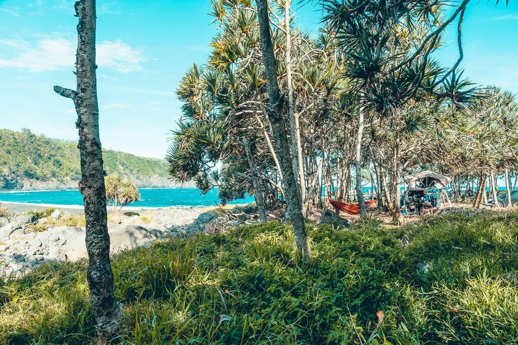 Une plage avec des arbres , un hamac et un 4x4 avec une tente de toit sur la plage de Vincendo à la Réunion.