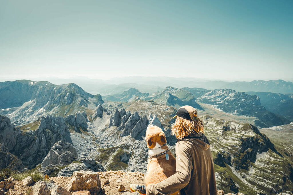 un homme et un chien devant une vue sur des montagnes au sommet du Bobotov Kuk dans le Durmitor au Monténégro